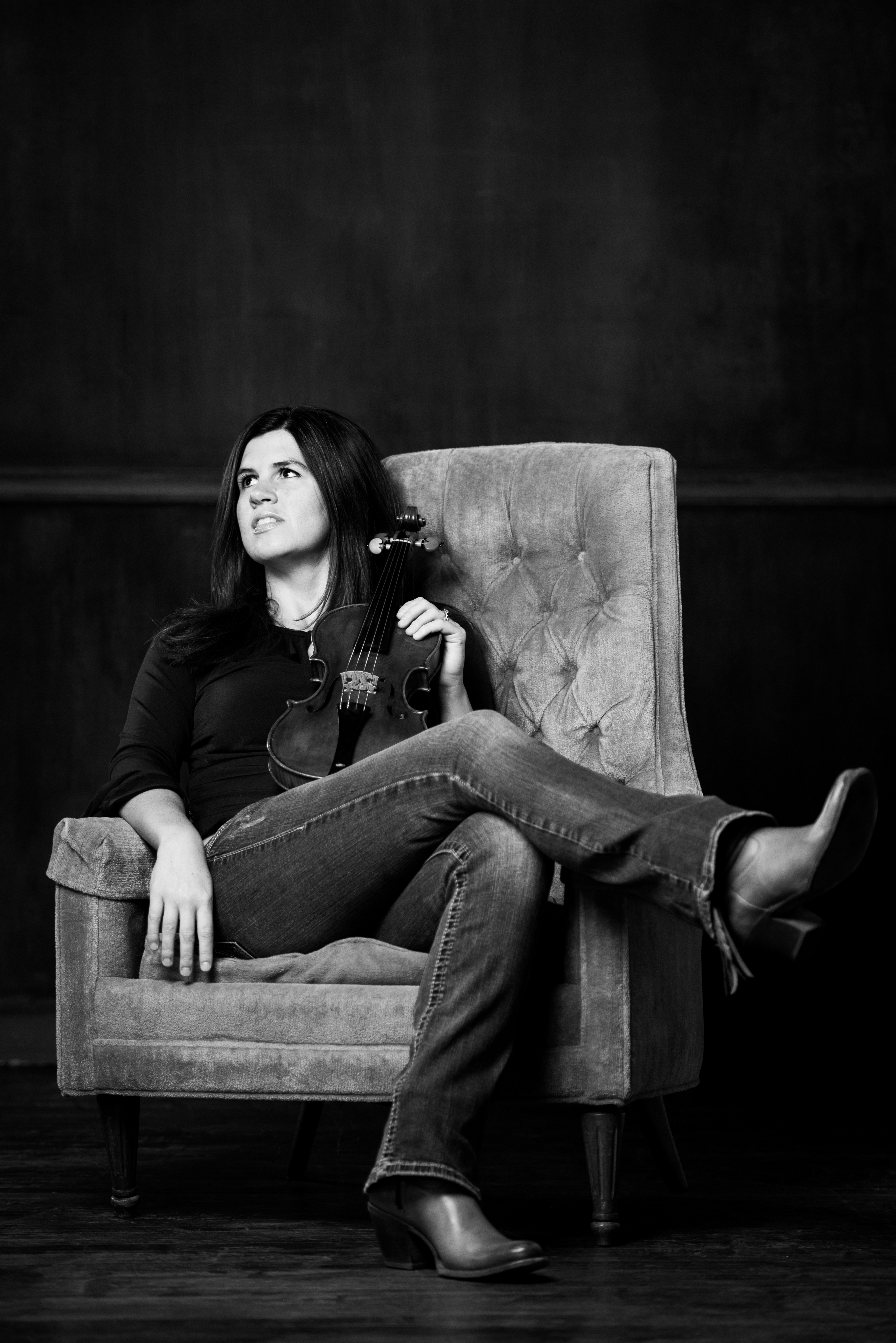 A woman with long dark hair sits in a chair holding her violin