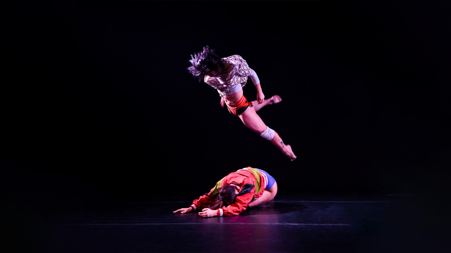 One performer leaps over the other who is on the ground.
