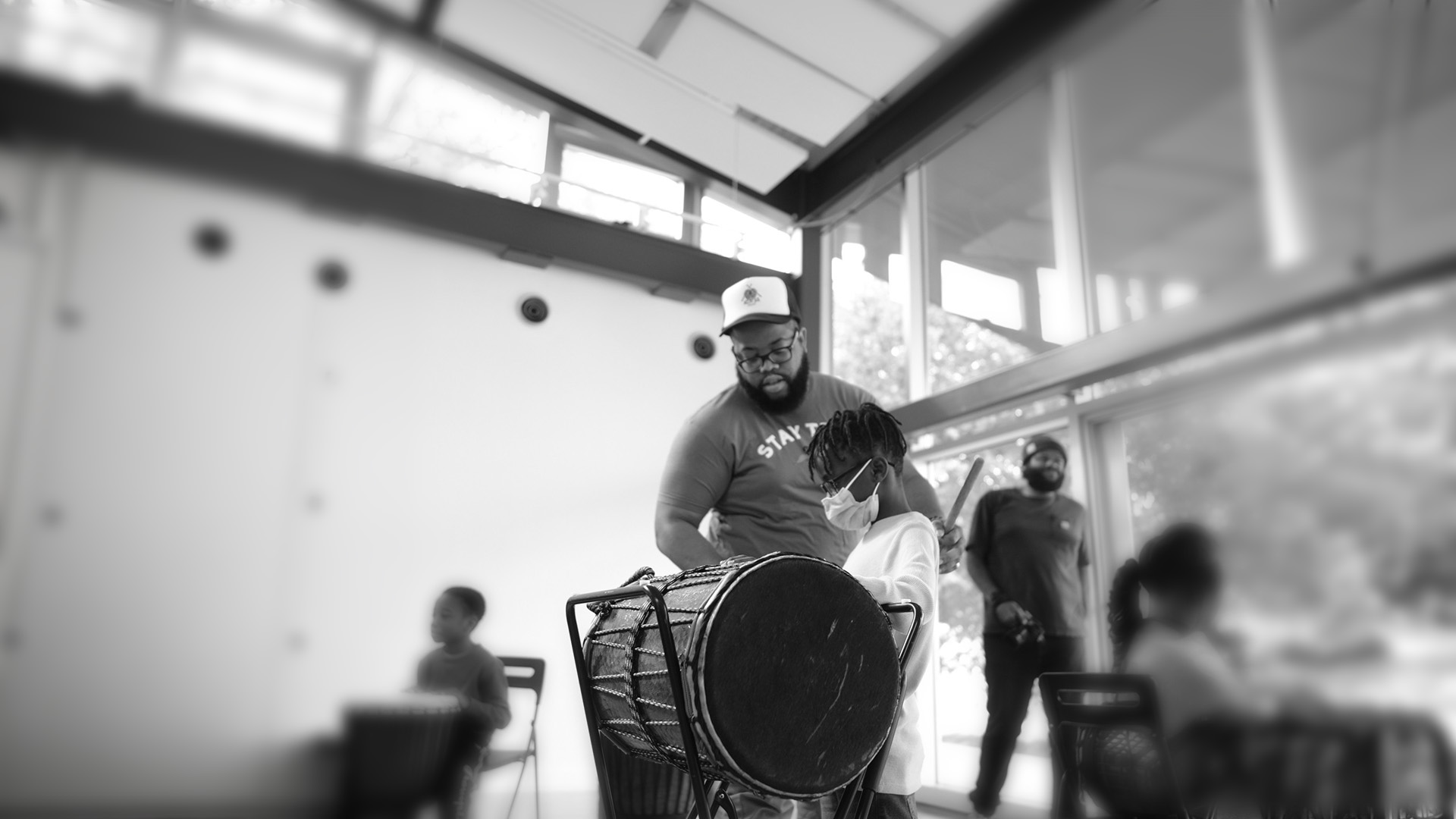 A Black man instructs a child on how to play a standing drum/