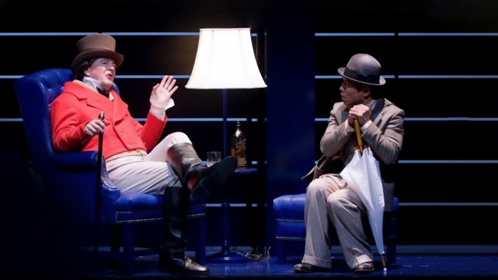 two actors sitting on stage in lounge chairs