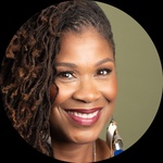 A smiling black woman with thick locks of hair, and brown eyes, and bold jewelry