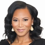 A black woman smiles warmly while looking at the camera. The image is in black and white.