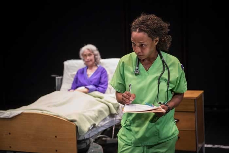  Brooks in green nurse scrubs, in the background Deanna Dunagan the patient  hospital gown and robe. 