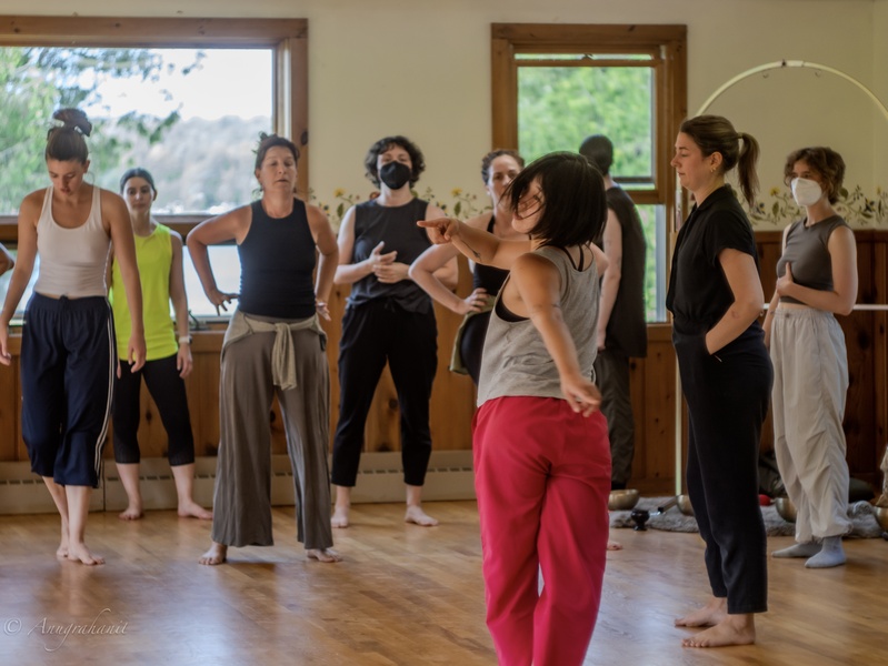  A Korean-American person with short black hair leads a dance class in a studio. 