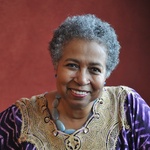 Black woman with short gray hair, brown eyes, smiling and wearing a colorful patterned top