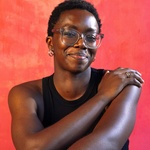 ebere in front of pink smudge backdrop, looking straight into the camera, giving themself a hug.