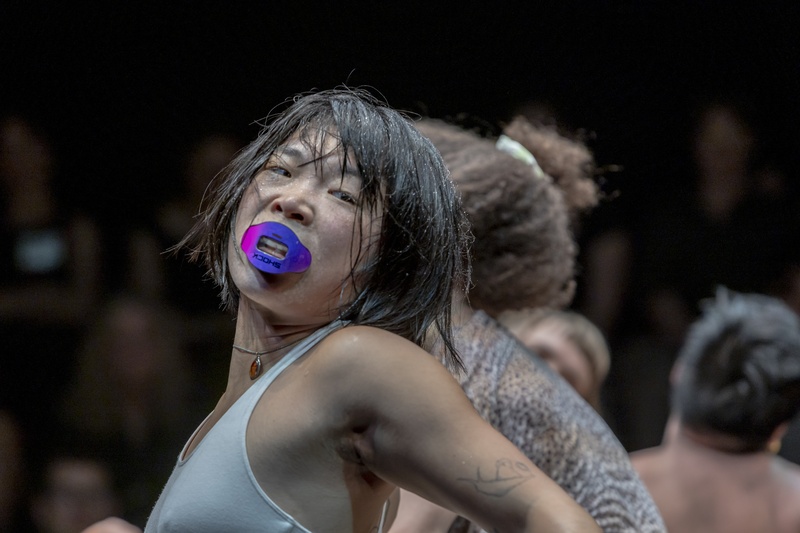  A Korean-American person with short black hair and a purple mouthguard turns while performing. 