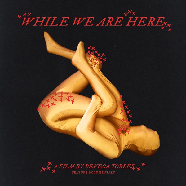  The poster features a gold-suited figure curled into a fetal pose against a black background, with red “X” marks. The title WHILE WE ARE HERE appears prominently at the top, with “A FILM BY REVECA TORRES” and “FEATURE DOCUMENTARY” below. 