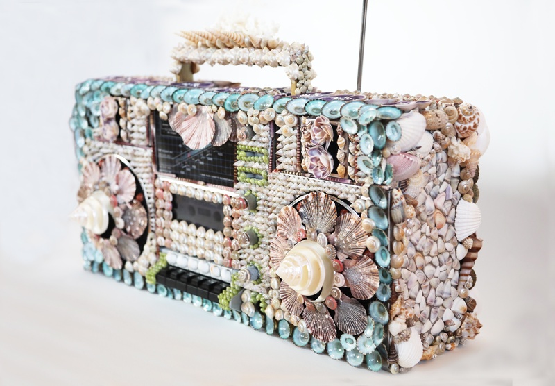 A boombox stereo covered with various seashells against a white background. 