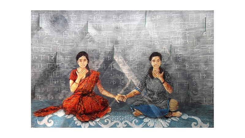  There are two girls sitting on a light blue mat, holding hands with each other and touching their own throats. 