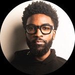 Black American male, pronouns: he/him, short curly black hair, with dark brown eyes and thick glasses.