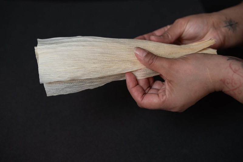  A close up of hands holding a tamale husk on a black background. 