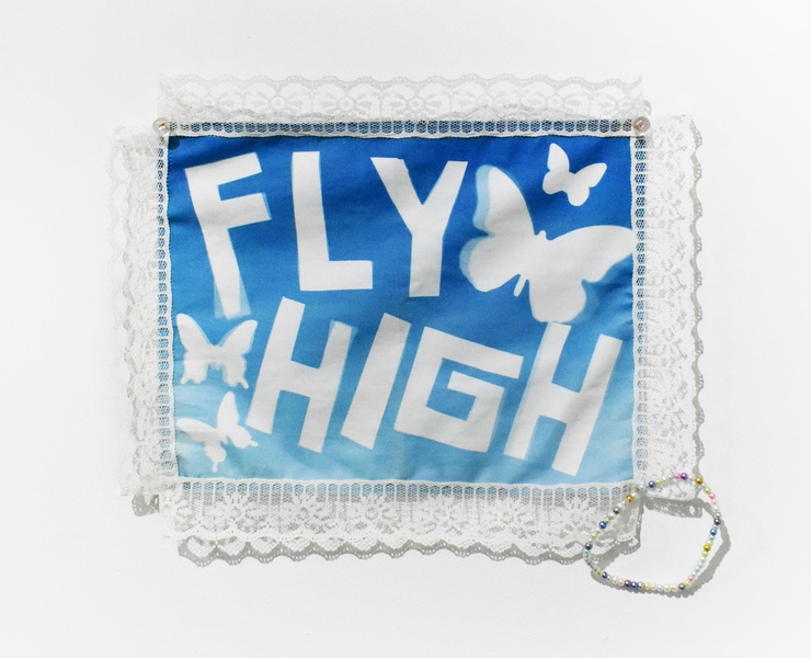  A blue textile hanging on the wall. It reads Fly High and there are butterflies surrounding the lettering. 