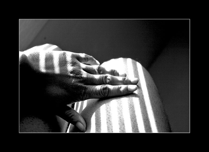  Black and white photo of the sunlight seeping through blinds in strips of light cascading across black skin 