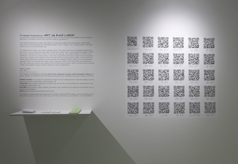  A white gallery wall with 30 QR codes pasted in a grid next to some wall text. 