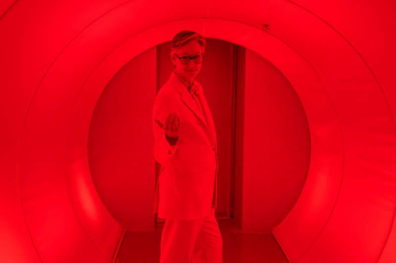  Kelli Simpkins in a red hued photo poses as David in Theater of the Mind, and invites the audience into an interior room. 