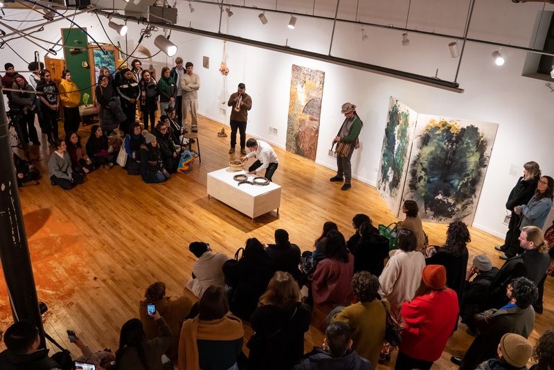  An audience watches a performer manipulate objects on a white table in a gallery. 
