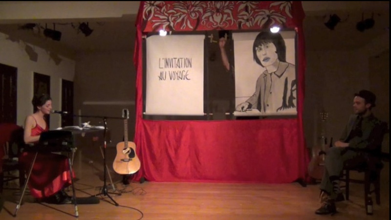  woman playing a Rhodes electric piano and singing in front of an illustrated scroll depicting a Baudelaire poem 