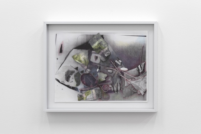  a drawing made on a photocopy. A grey, black, white, purple, and green art piece in a white frame hung on a white wall. The piece showcases various objects with splashes of green and pills of different sizes rendered in black, white, and grey. 