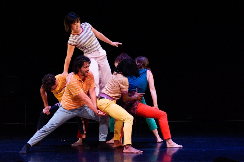  A group of performers lift one person up in a black space. 