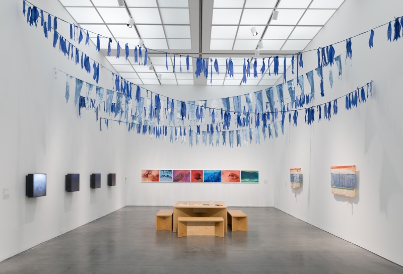  An installation view of a gallery exhibition featuring a string of blue reclaimed fabric flags. 