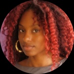 The image presents a Black woman with voluminous deep cherry red curly hair and brown eyes, photographed against a muted purple backdrop wearing a gray top and gold hoop earrings. She faces the camera with a relaxed posture and direct soft gaze expression
