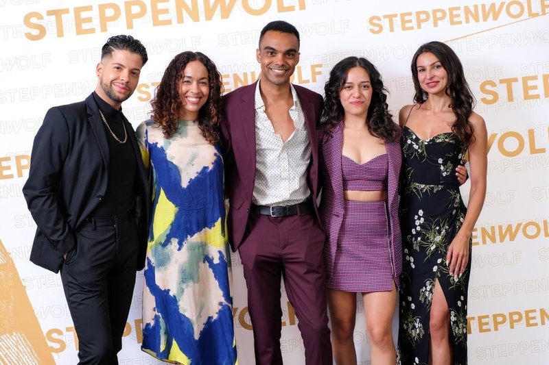  Five people post on a white backdrop with the word Steppenwolf detailed in gold font. 