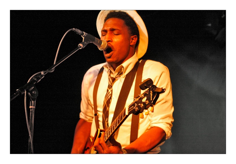  Photo of a black guitarist soulfully singing into a microphone 