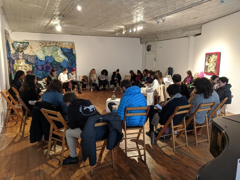  A group of workshop participants sitting in chairs arranged in a circle and doing a writing exercise with papers in their laps. 