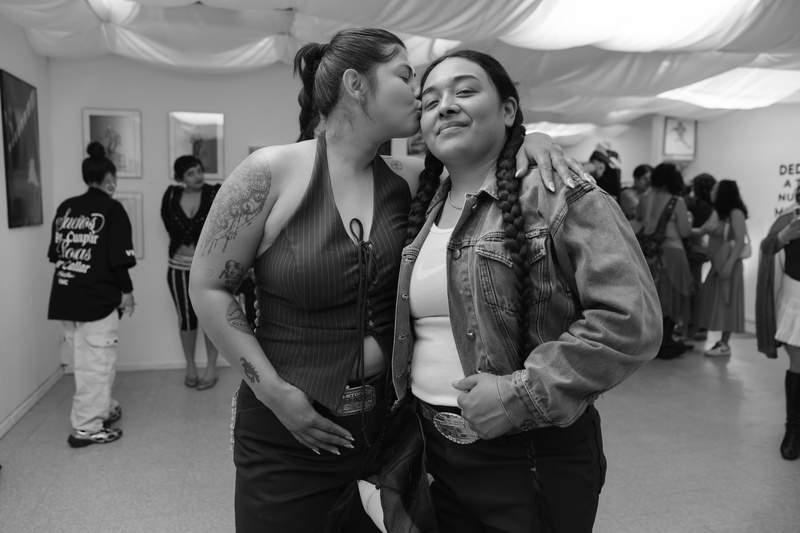  Two people post for a portrait in black and white. One person is kissing the other persons cheek. 