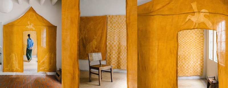  Instillation of a yellow fabric tent hung over a doorway. There is a person inside looking at checkered fabric. 