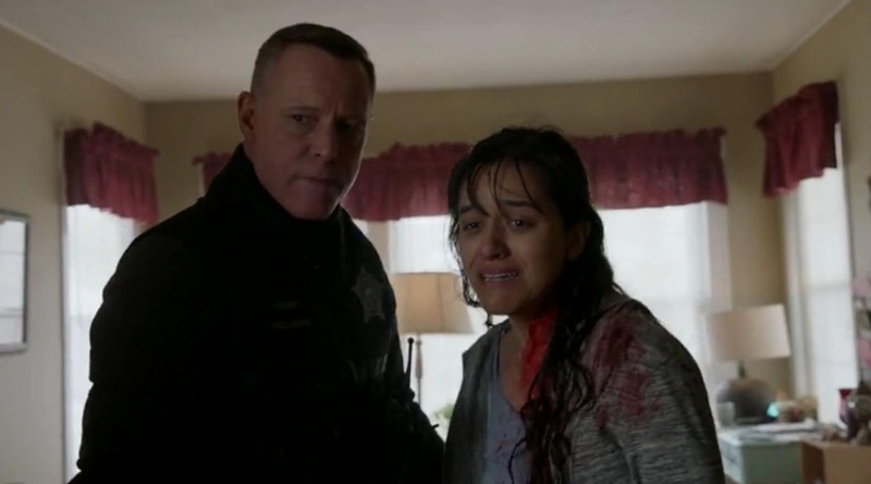  A still from a television show. Jason and Jocelyn are standing in a beige living room with red curtains. They are looking past the camera with scared expressions on their faces. Jocelyn has blood on her neck. 