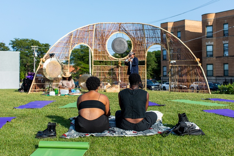  large half circle wood frame sculpture features woven strings, a wooden bridge, and a metallic gong 