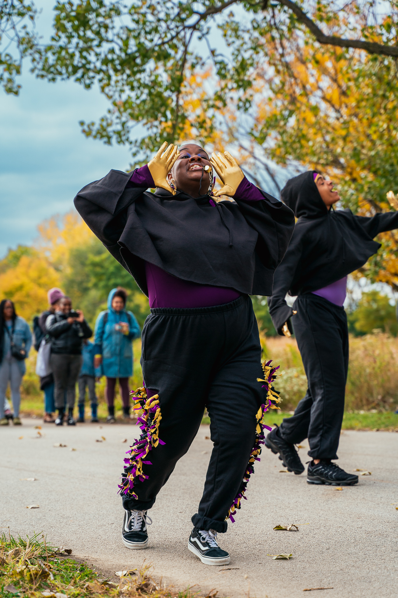  A dancer dressed in all black jumpsuit and gold gloves holds her hands up to her mouth to shout 